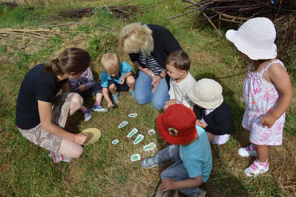 Des enfants et des adultes autour d'un atelier nature, assis dans l'herbe